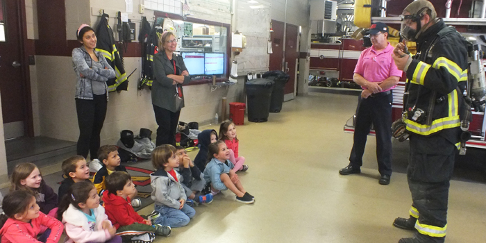 Preschoolers watching the fireman put on his safety gear